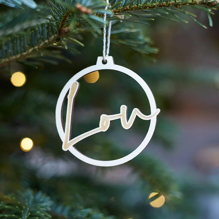 Een kerstbal uit hout gesneden met de naam Lou erin. Bal hangt in een kerstboom met lichtjes aan.